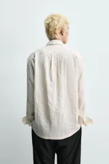 Camisa de corte relajado confeccionada en tejido fluido con textura jacquard de rayas verticales. Presenta cuello clásico, cierre frontal con botones, manga larga con puños abotonados y un bolsillo de parche en el pecho.