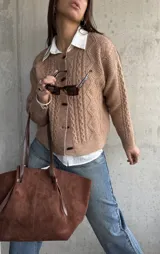 Cardigan de punto trenzado en color beige, con cuello redondo, cierre frontal de botones oscuros y mangas largas con puños acanalados.