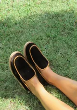 Mocasines de terciopelo verde oscuro, con ribetes en tono tostado y detalle de aplique metálico de un caballito en el talón. Poseen suela y taco bajo de madera.