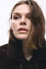 Campera oversized de doble faz con exterior de efecto gamuzado y forro interior de sherpa. Presenta cuello clásico, cierre frontal con botones, hombros caídos y bolsillos laterales insertados.