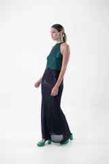 Vestido largo de fiesta con lentejuelas, compuesto por un top verde esmeralda con cuello halter y una falda negra ajustada con abertura lateral.