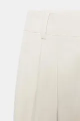 Pantalón de tiro medio con pinzas delanteras, bolsillos frontales y falsos bolsillos con solapa en la parte posterior. Presenta un diseño de pernera holgada que se estrecha hacia el tobillo, con cierre frontal de cremallera y botón.
