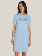 Vestido Tommy Hilfiger celeste de corte recto, con cuello redondo y mangas cortas. Presenta un logo script de la marca estampado en el pecho y la bandera de Tommy Hilfiger bordada en la manga.