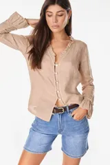 Blusa de lino italiano color beige con escote en V y detalles de volados en el cuello y los puños. Presenta cierre frontal con botones de nácar y mangas largas.