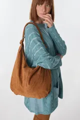 Bolso hobo de cuero gamuzado color marrón, con correa de hombro y cierre superior.