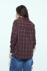 Camisa tipo leñadora de corte oversize, con estampado de cuadros en tonos negro y marrón. Presenta cuello clásico, cierre frontal con botones y mangas largas con puños abotonados.