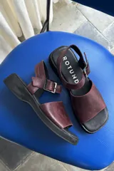 Sandalias de cuero color bordó, con suela plana y gruesa de goma negra, tira ancha en el empeine y tira ajustable con hebilla en el talón.