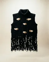 Chaleco tejido en lana merino color negro, con cuello alto y diseño sin mangas. Presenta aplicaciones decorativas en relieve de color crema y marrón que simulan figuras abstractas, y un ruedo terminado con largos flecos negros.