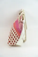 Bolso de playa o tote bag con diseño de patchwork en tonos rosados, naranjas y blancos. Presenta secciones con estampado de lunares rojos y secciones con tejido de rafia. Las asas son de cuerda trenzada.