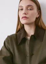 Chaqueta verde militar corta con cuello camisero de pana marrón oscuro, cierre frontal de botones, bolsillos aplicados en el pecho y diseño holgado.
