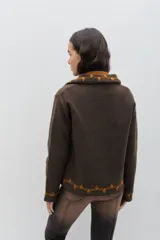 Chaqueta de lana merino hervida en color marrón, con diseño estructurado y cuello amplio. Presenta detalles de bordado artesanal en contraste color mostaza a lo largo del frente, cuello y puños, junto con botones forrados en la misma tela.