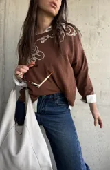 Sweater de punto color chocolate, de corte holgado, manga larga y cuello redondo con delicados bordados contrastantes en el frente.