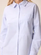 Camisa de manga larga con cuello clásico y cierre frontal de botones, confeccionada en tela de algodón con diseño de rayas verticales finas en color rosado y blanco. Presenta un bolsillo frontal en el pecho con detalle de etiqueta pequeña.