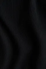 Top negro de manga larga, tejido en punto acanalado, con escote amplio tipo barco que deja los hombros al descubierto y un leve escote en V. El bajo y los puños terminan con un ribete fino de volados.