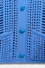 Chaleco azul de punto calado con cuello redondo, sin mangas, cierre frontal con botones y dos bolsillos de parche en la parte delantera.