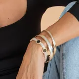 Pulsera de diseño articulado en plata y oro, con eslabones de malla metálica y dijes circulares con piedra ónix negra en el centro.