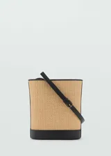 Bolso tipo bucket con cuerpo de rafia y base, bordes y correa ajustable en color negro. Presenta un diseño estructurado de tamaño mediano con cierre regulable.