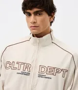Campera de tejido técnico color beige con detalles de costuras en contraste color marrón. Presenta cuello alto, cierre frontal con cremallera, mangas largas con puños elásticos y estampa frontal con texto. Incluye un detalle bordado en la manga.
