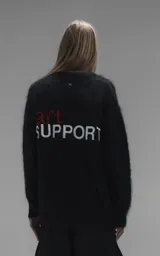 Sweater de punto negro de textura suave, con cuello redondo y diseño oversize. Presenta un bordado en relieve en la parte trasera con las palabras 'art support' en color rojo y blanco.