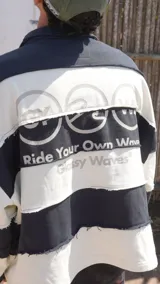 Buzo estilo rugby de corte oversize, con diseño de rayas horizontales anchas en blanco y negro. Presenta cuello tipo polo, costuras expuestas con efecto desflecado y el logo de la marca estampado en el pecho.