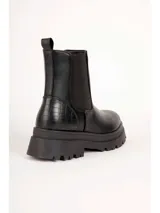 Bota de caña baja tipo Chelsea color marrón, con paneles elásticos laterales y suela track negra con plataforma dentada. Presenta textura en relieve en la parte trasera del talón.