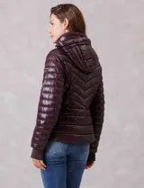 Campera puffer de acabado satinado en color marrón oscuro. Presenta un diseño capitoneado con líneas en V, cierre frontal metálico, capucha fija y puños internos de tejido elastizado con abertura para el pulgar. Incluye bolsillos laterales con cierre invisible y logo metálico en la manga.