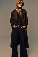 Abrigo largo color marrón oscuro con efecto ante, cuello solapa, manga larga con trabillas en los hombros y bolsillos delanteros de vivo. Presenta un bajo con abertura en la espalda y cierre frontal cruzado con botones, complementado con un cinturón a tono.