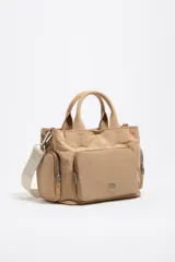 Bolso bandolera Pocket Bimba Y Lola de tamaño mediano, color tostado, confeccionado en nylon con estructura blanda, doble asa de mano y correa de tejido. Incluye un bolsillo exterior frontal con cierre y el logo metálico de la marca.