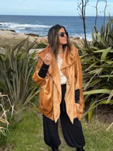 Campera oversize de abrigo color camel en tejido suave con efecto gamuzado, con gran capucha envolvente que puede usarse como bufanda, bolsillos laterales y puños elastizados negros.