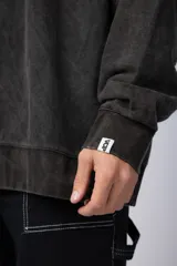 Buzo de cuello redondo y corte oversize, confeccionado en tela friza con efecto de teñido artesanal desgastado. Presenta un estampado pequeño en color verde lima en el pecho y una etiqueta pequeña en el puño.