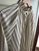 Camisa de rayas verticales, color vainilla con líneas oscuras, cuello alto con volados y botones frontales. Cuenta con mangas largas abullonadas y puños anchos abotonados.