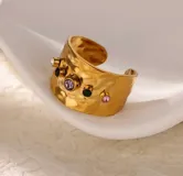 Anillo ancho de acero quirúrgico con textura martillada y detalles de piedras incrustadas de colores. Diseño ajustable.