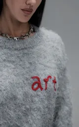 Sweater de punto texturizado color gris, con cuello redondo y diseño oversize. Presenta un bordado en relieve en la espalda con la frase 'art SUPPORT' en letras rojas y negras.