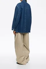 Chaqueta de denim azul de corte recto y holgado, con cuello camisero, cierre frontal de botones y cuatro bolsillos de parche (dos en el pecho y dos en el bajo).