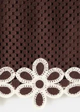 Falda corta de tejido crochet color marrón con detalles de flores blancas en el borde inferior. Silueta recta y forro interior.