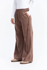 Pantalón de corte ancho y relajado en color marrón, con cintura elástica, bolsillos laterales y costuras verticales decorativas en contraste a lo largo de las piernas.