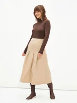 Falda midi de color beige, con diseño de tablas frontales y cierre lateral con botones decorativos. Presenta un corte estructurado y tiro alto.