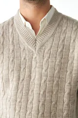 Chaleco de punto color beige con diseño de trenzas, escote en V y sisas amplias.