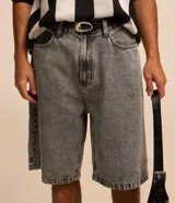 Bermuda de jean estilo baggy, color negro gastado, con bolsillos, cierre de botón y cremallera, y pespuntes contrastantes.