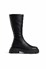 Bota de caña alta color negro, confeccionada en material elástico con acabado mate. Presenta una suela track robusta y dentada, con un diseño minimalista sin cierres visibles.