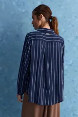 Camisa de calce relajado con cuello clásico, mangas largas con puños elastizados y rayas verticales que aportan un estilo atemporal. Su diseño liviano y versátil cuenta con estampado floral verde sobre fondo de rayas celestes y blancas.