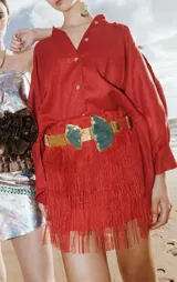 Minifalda roja con flecos de rafia y cinturón dorado con apliques de piedra verde.