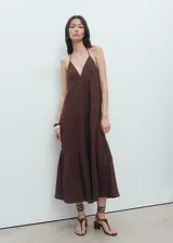 Vestido midi marrón de 100% algodón, sin mangas, con escote en pico y tirantes finos que se atan al cuello. Presenta diseño evasé con detalles fruncidos escalonados y textura.