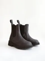 Bota tipo Chelsea de caña media, confeccionada en cuero negro con acabado mate. Presenta paneles elásticos laterales, tiradores traseros y suela track robusta con plataforma dentada.