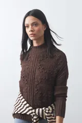 Polera de tejido de punto color marrón, con cuello alto y diseño de textura con relieves y trenzas. Posee mangas largas con puños acanalados.