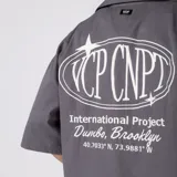 Camisa de manga corta color marfil, corte boxy, con cuello camisero, cierre frontal de botones y pequeño bordado marrón en el pecho con las siglas VCP.