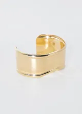 Pulsera brazalete rígido dorado con diseño ondulado.