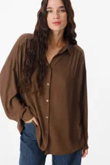 Camisa de corte oversize color chocolate, con cuello clásico, cierre frontal de botones y mangas largas con puños abotonados. Presenta un diseño fluido y holgado con sutiles frunces en los hombros.