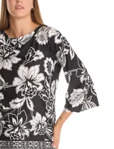 Blusa de seda fría con estampado floral en blanco y negro. Presenta cuello a la base, mangas tres cuartos amplias y ruedo con abertura lateral decorada con botones.