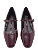 Zapato plano tipo Mary Jane, color bordó, de punta fina y tira en forma de T con hebilla metálica dorada ajustable.